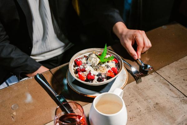 Man sat at table and holding a spoon next to an acai bowl topped with seasonal berries, banana, house made granola, and coconut