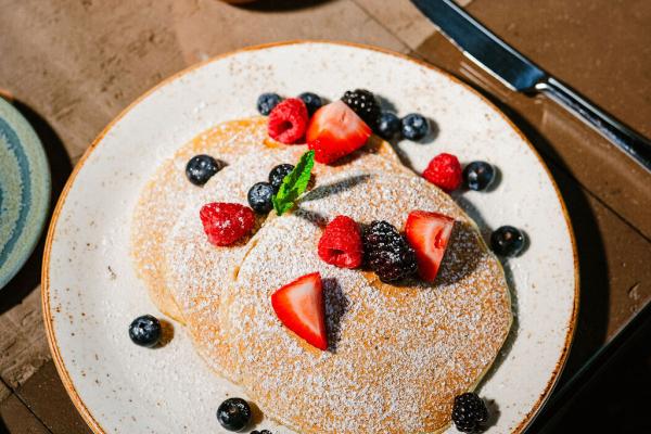 three large, fluffy pancakes on round, white plate and topped with powdered sugar, strawberries, and blueberries