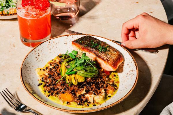 large salmon and quinoa dish and roasted chciken dish placed side by side on round, white tabletop