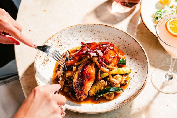 person using fork and knife to cut into Pan Roasted Chicken dish that is placed on round white tabletop