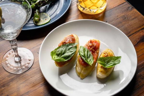 toasted crostini topped with tomato and garlic on a metal plate, garnished with fresh basil leaves.